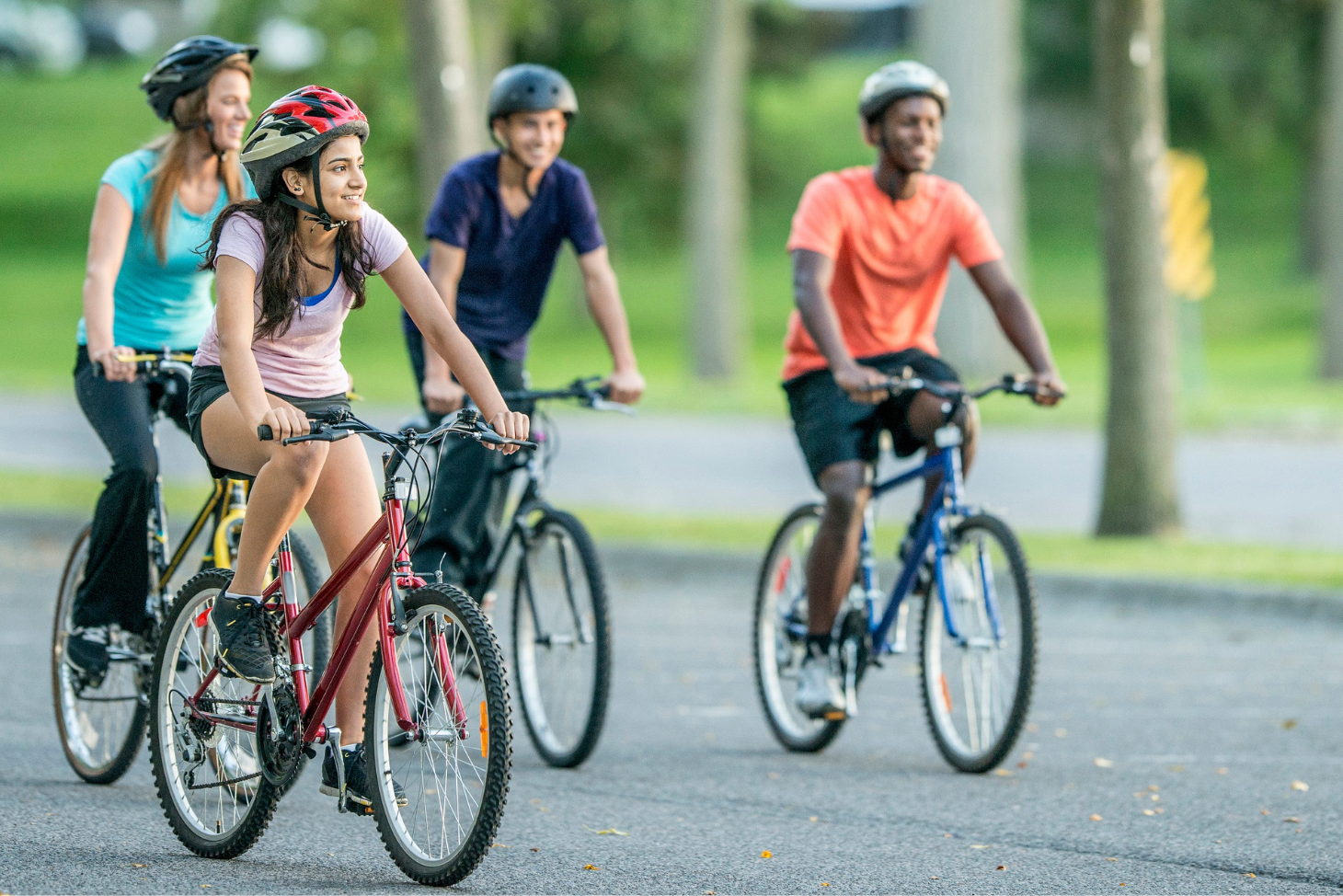 Four teens riding bikes on a street while wearing helmets