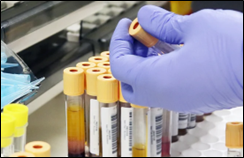 Image of gloved hand holding vials of blood in a lab