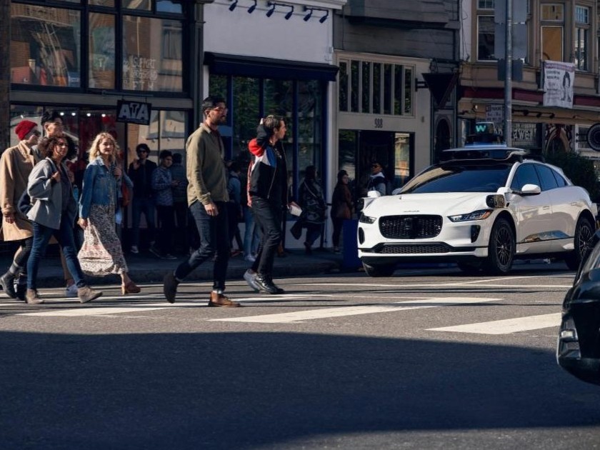 People crossing the street in front of a Waymo vehicle
