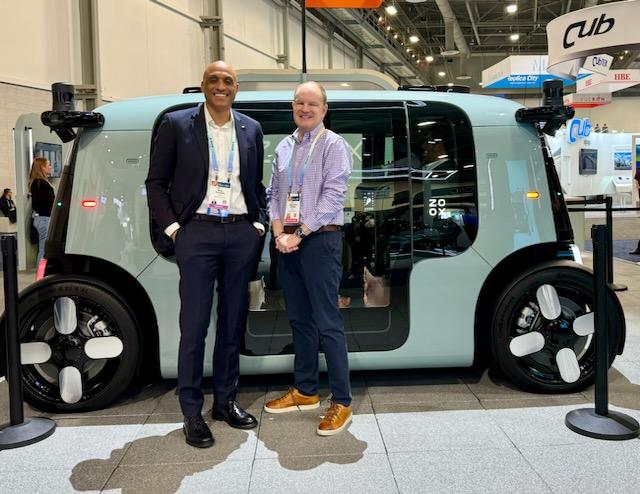 Image of two men standing in front of a futuristic-looking driverless car