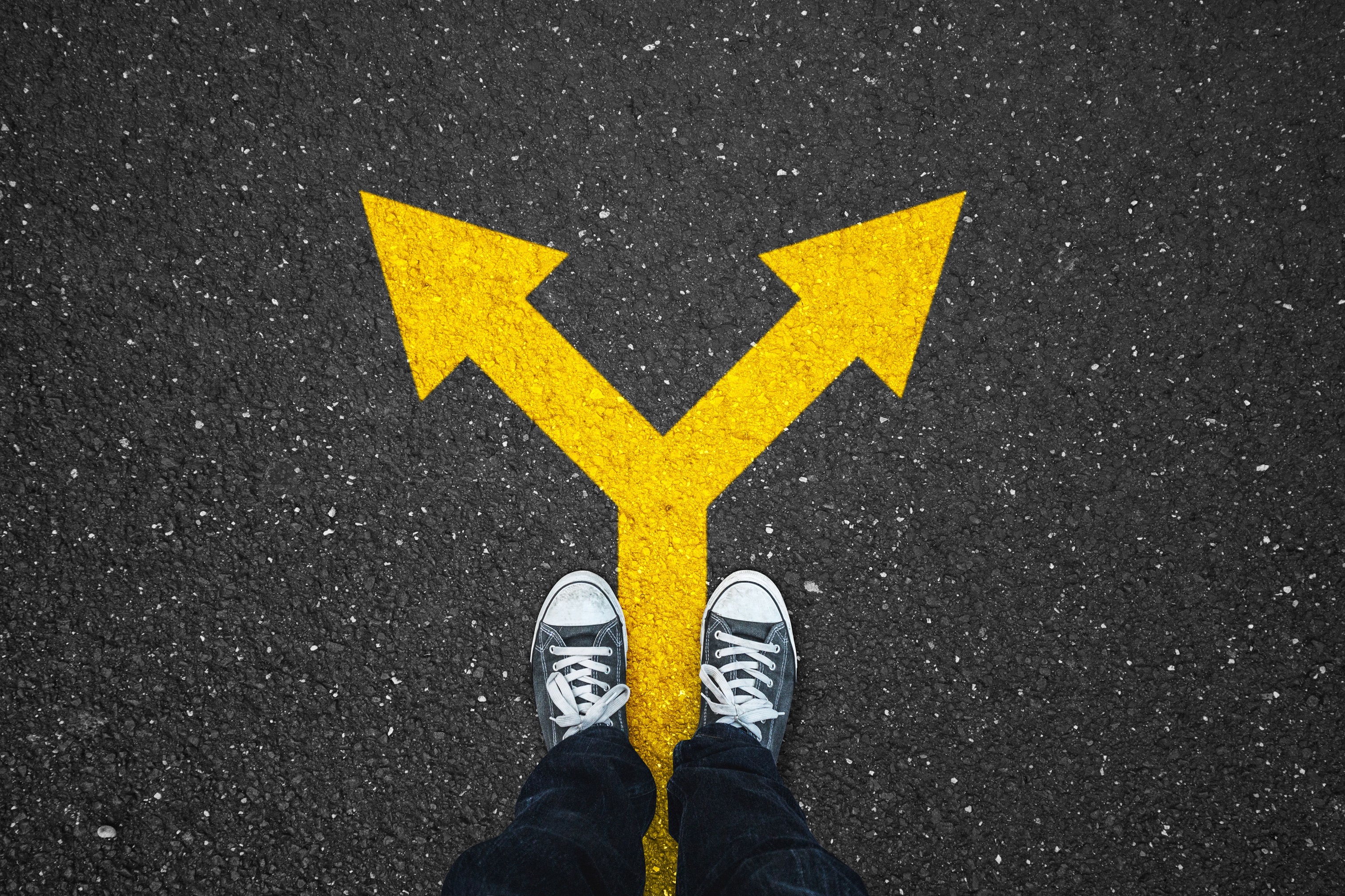 Image of two feet standing on pavement with a yellow arrow pointing in two different directions