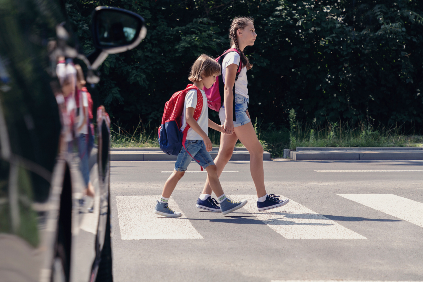 Two children crossing a road in a crosswalk with a car nearby